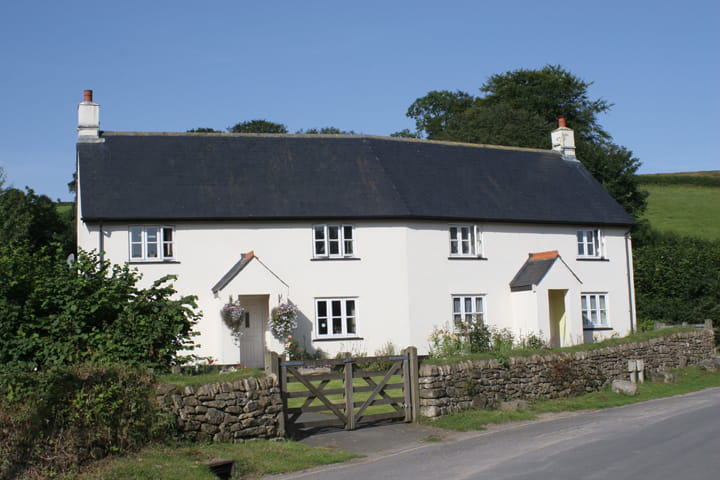 picture of a pair of white thatched cottages with a stone wall in front, taken on a sunny day
